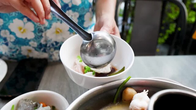 A Person Ladling Hot Tom Yum Seafood Soup into a White Bowl