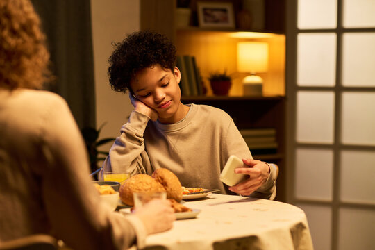 Teenager boy checking smartphone during family dinner, showing screen distraction and reduced communication at home. Useful for parenting, digital wellbeing, screen time campaigns
