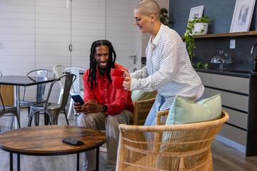 Naklejka premium Diverse coworkers wearing red shirt, handing red mugs on coffee table and checking phone in lounge