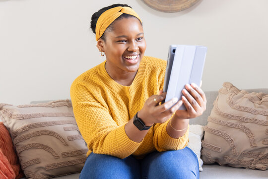 African American teen wearing mustard sweater on living room sofa holding tablet in folio case