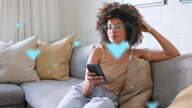 Woman tapping phone on sofa using dating app and causing blue hearts passing over frame