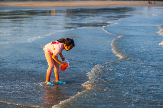 Young girl with orange bucket collecting shells at the ocean shore