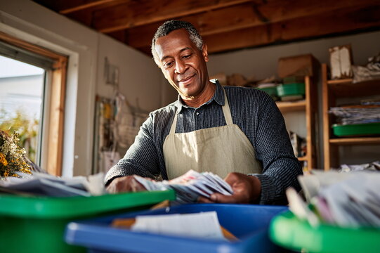 Middle-aged Black man with content expression sorting items in sunlit workshop