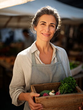 Smiling Hispanic woman farmer with fresh produce in a crate at an outdoor market