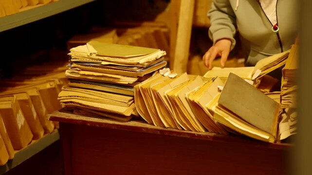 Archivist Sorting Through Stacks Of Old Paper Files In Storage Room. Information Management And Data Recovery