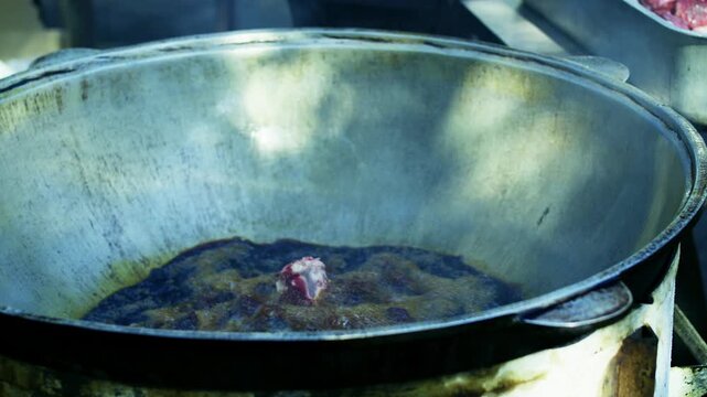 Chef placing large pieces of raw meat into boiling oil in kazan for plov