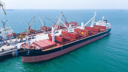 Obraz premium a large bulk carrier ship docked at an industrial port terminal for cargo loading. Concept of maritime logistics, global shipping industry, and international trade supply chain.