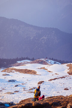 A person sitting on a rocky hilltop with a breathtaking mountain landscape in the background near Tungnath temple, Uttarakhand, India
