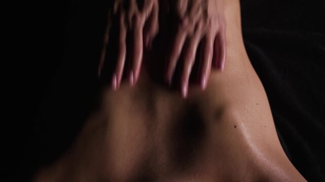 Masseur gives back massage to young naked woman lying on her stomach. View from above.