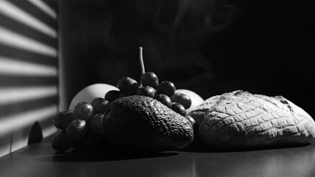 Black and white still life with avocado, grapes, bread, and eggs, smoke and shadows