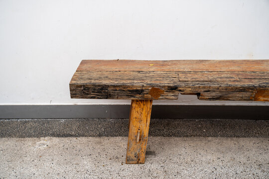long wooden bench in the public and white cement wall background. Art and handmaid.