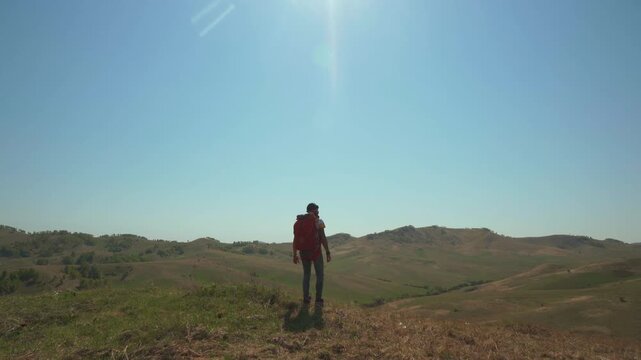 A man walks across a field with a parachute pack on his shoulders. A lover of extreme sports on a solo hike in the countryside.