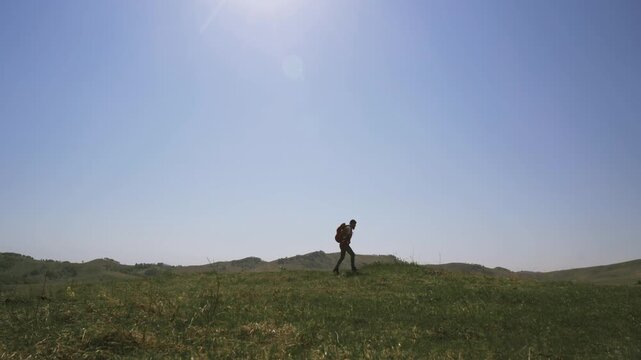 A man walks across a field with a parachute pack on his shoulders. A lover of extreme sports on a solo hike in the countryside.