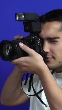 Young male photographer holding a professional dslr camera and taking photos during a studio photoshoot with a blue screen background
