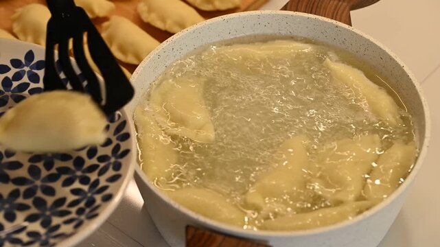 Christmas pierogi cooked in water and oil, taking cooked pierogi out of the pot on the stove, close-up, real time