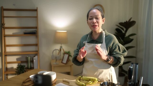 Senior woman livestreams cooking from home on smartphone, highlighting active aging and digital lifestyle. Reflects social media, content creation, creativity, and senior lifestyle.