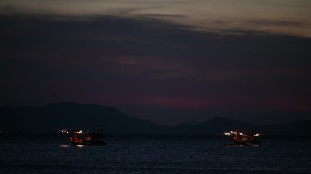 Fishing boats continue through darkening water at Tubkaek Beach
