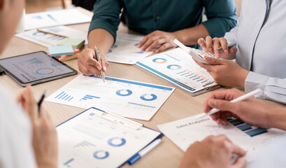 Obraz premium Professional business team collaborating on financial data and sales analytics using a calculator, tablet, and printed charts during a productive office meeting.
