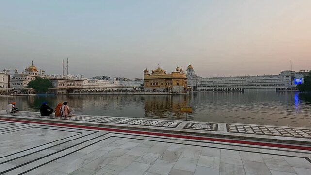Serene evening view of the Golden Temple (Harmandir Sahib) in Amritsar, Punjab, India, reflecting beautifully in the sacred Amrit Sarovar, with devotees sitting peacefully in the foreground.