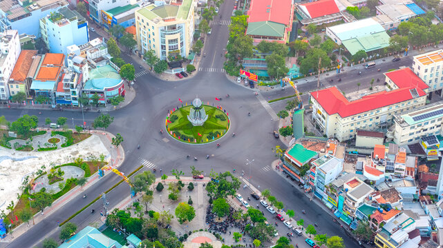 Aerial view of a busy urban roundabout in Nha Trang city, Vietnam, where roads converge around a landscaped traffic circle. Dense residential neighborhoods, colorful rooftops