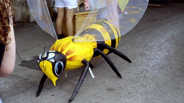 Large decorative bee sculpture displayed at outdoor event with children nearby creating playful colorful scene suitable for festival family activity and public space