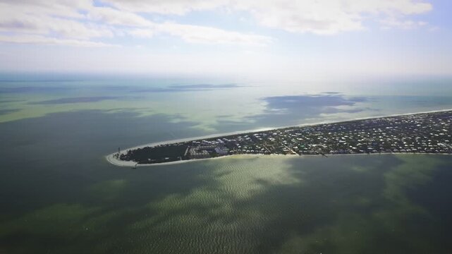 A cinematic, high-flying wide-angle aerial drone shot orbiting over the bayside of the historic Sanibel Island Lighthouse and the eastern tip of Sanibel Island, Florida, with bright coastal shoreline.