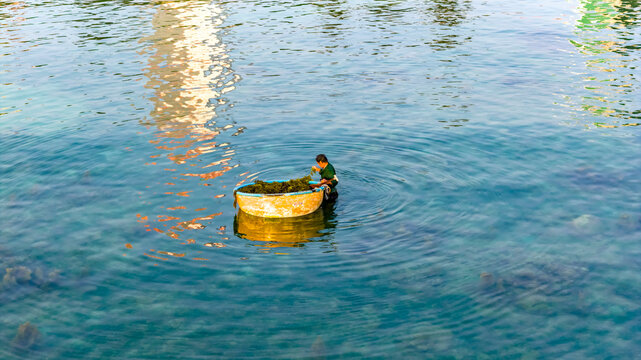 A peaceful coastal moment in Nha Trang, Vietnam where a fisherman sits beside a traditional round basket boat (coracle) floating on clear turquoise water. 