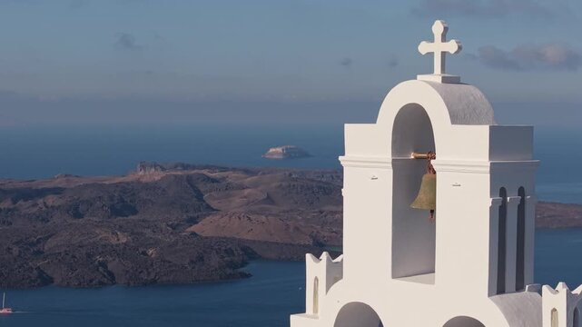 Drone orbit of a white chapel belfry in Santorini with the caldera and volcano in the background, capturing iconic architecture and the island&rsquo;s dramatic volcanic landscape.