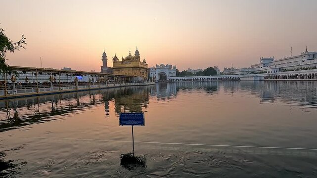 Beautiful sunrise view of the Golden Temple (Harmandir Sahib) in Amritsar, Punjab, with warm sky tones reflecting in the sacred Amrit Sarovar and pilgrims walking along the causeway.