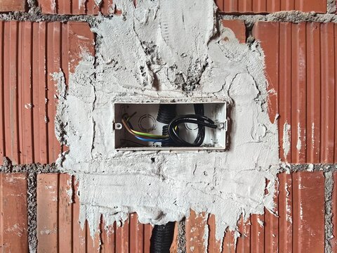 Electrical junction box with cables inside a house under construction. The photo focuses on the junction box with incoming and outgoing electrical wires. Exposed cables, unfinished wiring, and a plast