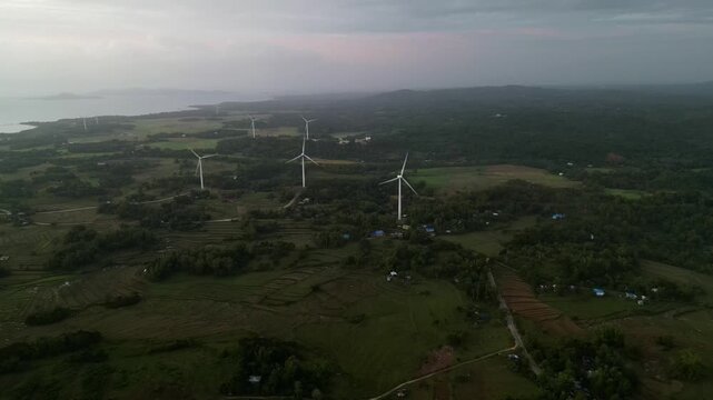 Rows of wind turbines stretch across vast farmland under a dusky sky in Guimaras, capturing a blend of nature and technology. Suitable for environmental and energy projects.