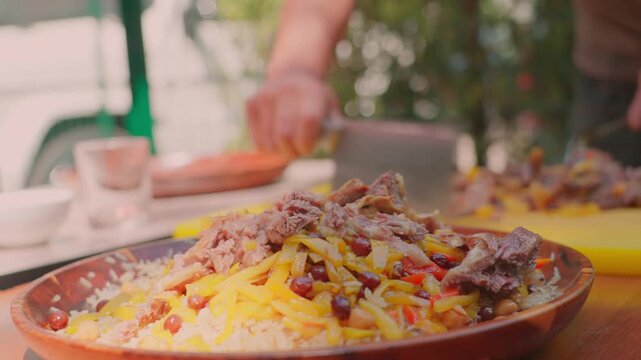 Chef adds boiled meat to Uzbek plov served on a wooden lagan, close-up