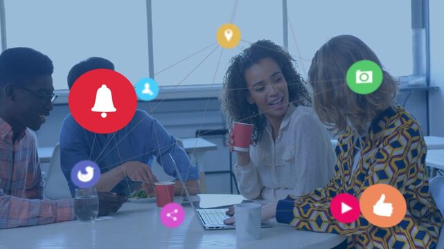 Team sitting at table, typing and tapping, spawning social icons linking coworkers for marketing