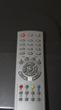 Silver television remote control with colorful buttons on dark surface