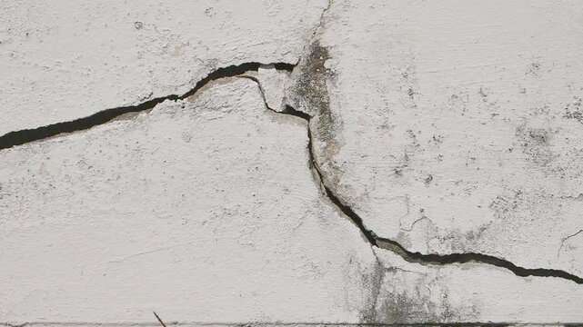 A deep horizontal crack on an old, weathered white wall with mold and moisture stains. Concept of building damage and aging structures.