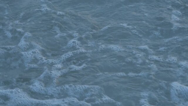 Slow motion of white ocean foam and sea spray splashing on the shore. Detailed view of water bubbles and turquoise sea water.