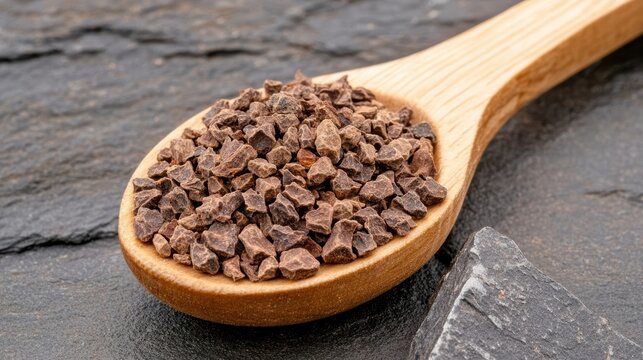 Natural cocoa nibs on wooden spoon.