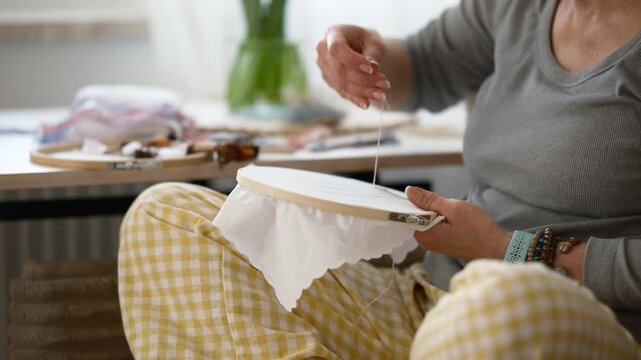 Woman focuses on drawing a design for embroidery using a pencil while sitting at her crafting table with supplies nearby
