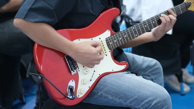 Red electric guitar held by player. Hands strumming with focused energy. 