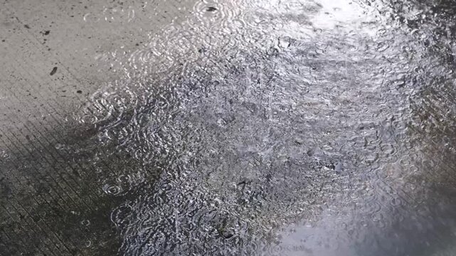 Raindrops strike a wet, textured surface. Water flows across a dark, ribbed material.
