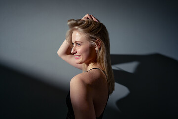 Fototapeta premium Positive young blonde woman posing indoors, illuminated by natural light, creating dramatic shadow. Highlighting happiness, beauty, and creativity.