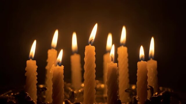 Close-up of multiple lit candles flickering in darkness.