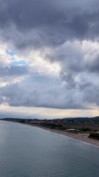 Vertical aerial of Acharavi beach in Corfu, Greece, moody storm clouds gathered over the calm Mediterranean sea and sandy coastline