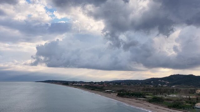 Dramatic storm clouds and sun rays over Acharavi coastline in Corfu, Greece, aerial tracking shot of sandy beach, Mediterranean sea, and coastal village