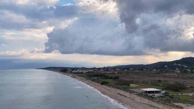 Aerial view of Acharavi beach in Corfu, Greece under a dramatic cloudy sky, scenic Mediterranean coastline with calm sea waves and green landscape