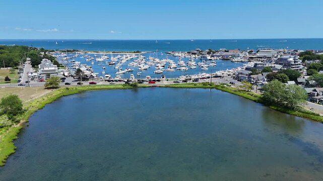Aerial drone view of Martha&rsquo;s Vineyard in Dukes County, Massachusetts, with calm coastal pond in foreground and busy harbor filled with boats along Atlantic shoreline on sunny day. Flyover shot.