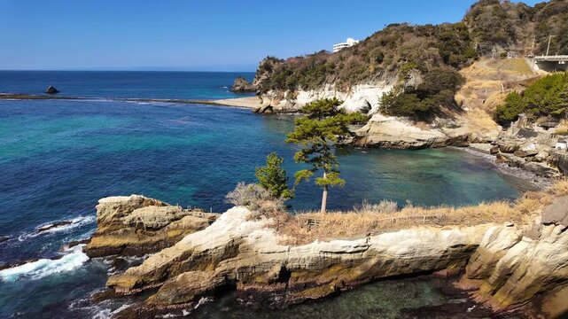 A scenic panoramic pan showcasing the stunning turquoise waters of Dogashima, Japan. The shot captures a rocky island and the famous Tombolo land bridge