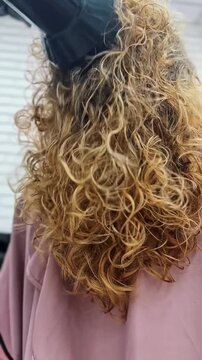 Professional hairdresser drying woman's curly blonde hair with a diffuser attachment in salon vertical video