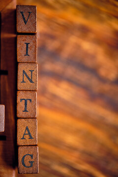Vertical row of vintage wooden letter stamps spelling VINTAG on a rustic, blurred wood background.
