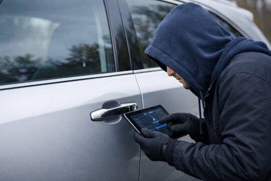 Man in hoodie using tablet device to hack parked car door lock system. Ai generative